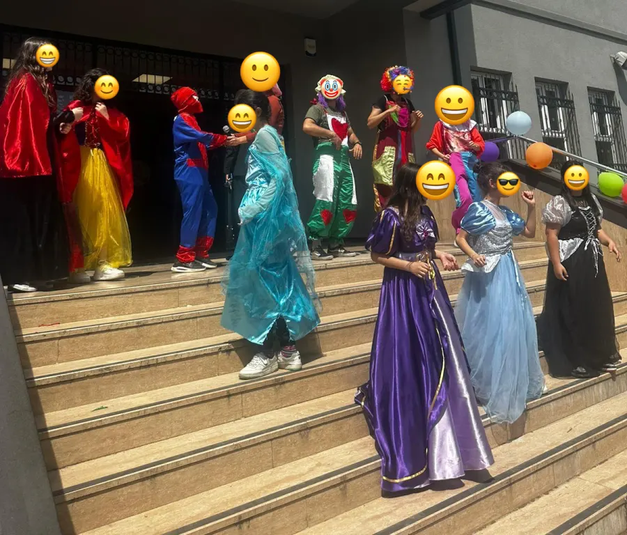 Okul şenliğinde kostümlü karakterler ve çocuklar, yüzler emojiyle kapatılmış